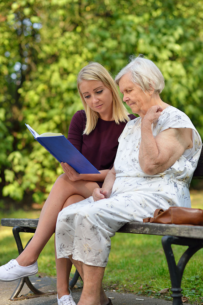 Young woman reading a book elderly woman in the park.